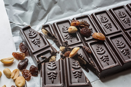带有坚果和葡萄的巧克力棒食品葡萄干糖果包装可可款待巧克力黑板棕色背景图片