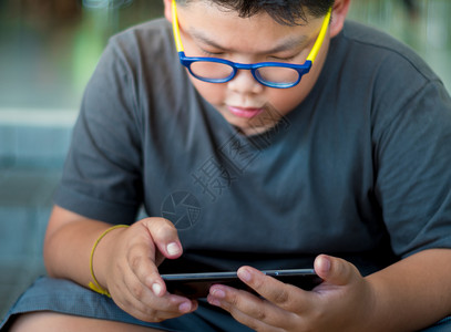 亚洲男孩玩智能手机游戏时面相很严肃互联网电话技术男生孩子们眼镜背景图片