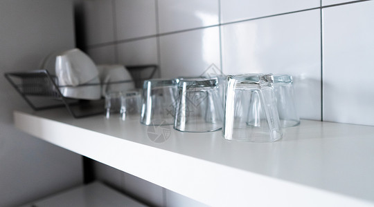 白色上的搁板玻璃用于存储和展示的宽大厨房搁板和壁架 现代斯堪的纳维亚厨房的白色木架和经济型轻型餐具架 配有餐具 杯子和玻璃杯 贴在墙砖上电器用具背景