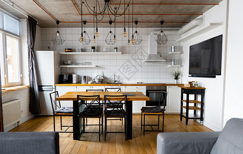 现代斯堪的纳维亚式厨房室内设计 大木桌和椅子与浅色木地板 明亮的白色墙壁和带电视 电器和悬挂灯泡的家具橡木桌子架子奢华日光农家餐背景图片