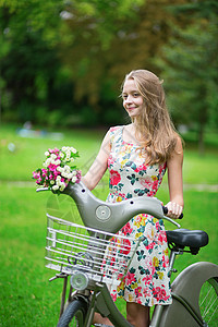 女孩骑自行车在农村骑自行车的漂亮女孩在乡下女孩白色闲暇公园女士假期绿色花朵裙子背景