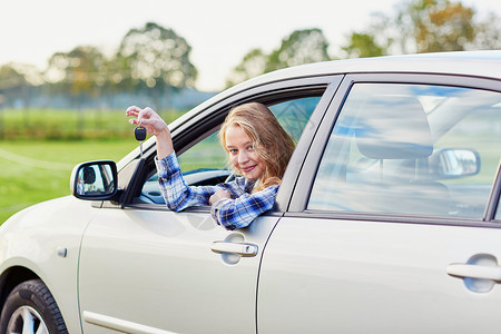 开小汽车的女孩年轻司机拿着钥匙向车窗外看的年轻司机运输汽车测试驾驶日落腰带交通窗户旅行贷款背景