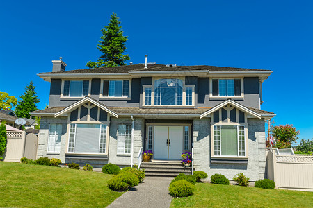 温哥华郊区的大家族住宅 在蓝天背景下门廊窗户院子天空家庭入口不动产草地灌木丛建筑学背景图片