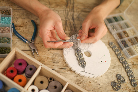 线条珠宝素材近身的雌性手 用木制桌边的木板 工具 线条 天然石头和彩珠做一个马卡梅手镯 并配有Kumimimio工作手工业手工蕾丝配饰矿物针背景