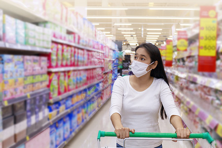 亚裔女性在超市戴面罩推车女士购物中心消费者顾客持有者口罩店铺食物大车女孩背景图片