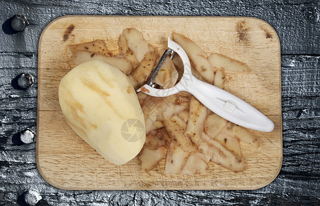 马铃薯削皮器Raw马铃薯在木制切削板上剥皮 有磨皮机背景