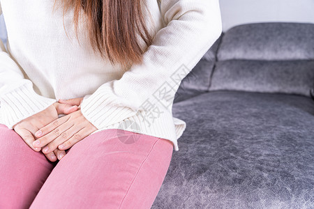 妇女在家中坐在沙发上时 手握着她的膝盖 肚子疼 吃不饱 在医疗或日常生活概念方面女孩疾病腹胀伤害疼痛便秘女士身体经期腹痛背景