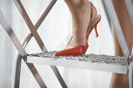 红高跟鞋身穿红色高脚鞋 站在铝上站立的红高铁皮鞋的妇女一人身体女士高跟鞋工作室影棚梯子设计一部分办公室背景