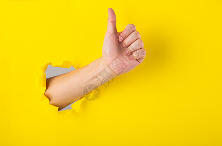 黄色大拇指手举着拇指在破洞中竖起标志黄色手势手指背景可用空间背景