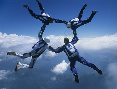 四个天空飞人手牵手对着云四个人男人队形运动降落伞风险极限自由落体头盔男士背景图片