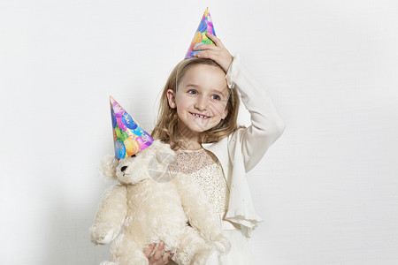 党生日的素材生日快乐的年轻女孩 戴着党帽 与泰迪熊在彩色背景背景