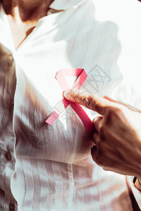 尾随一个老女人用粉色丝带指着胸口治愈乳腺癌检测疾病帮助胸部健康生存世界女性背景