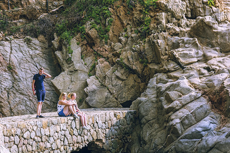 两个女孩和一个男人在靠近山的石桥上(Lloret)背景图片