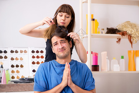 年青男子看女理发师深色梳子造型师男性沙龙金发头发顾客发型护理背景图片