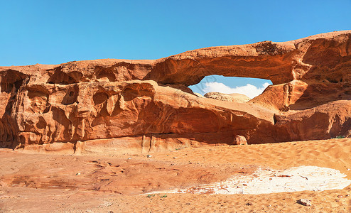 在Wadi Rum沙漠的小弧或小岩窗形成时 阳光照耀着红尘和岩石 蓝天在上方背景