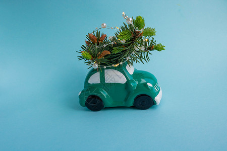 绿色玩具汽车小猪银行 在屋顶上携带一棵圣诞树 蓝底有园地背景图片