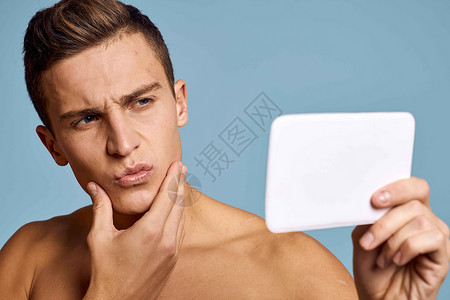 一个男人用蓝背景的眼神 照着镜子看脸剃须身体奶油温泉护理微笑男生治疗皮肤浴室背景图片