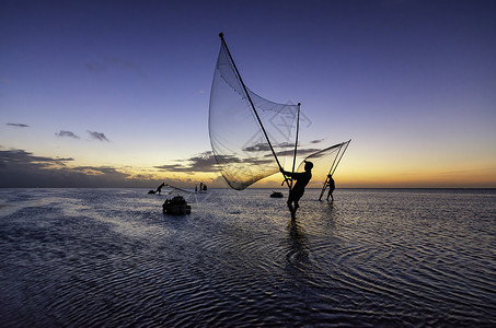 黑影渔民在清晨渔夫文化太阳橙子蓝色钓鱼日落海洋海滩反射背景图片
