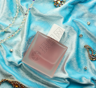 粉红色全瓶 有霜冻的玻璃香水 躺在蓝色背面上石头化妆品香水厂瓶子液体女性空白奢华商品胸针背景图片