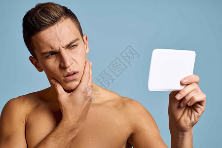 一个男人用蓝背景的眼神 照着镜子看脸男生奶油剃须成人治疗身体头发男人浴室眼睛背景图片