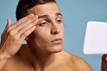 一个男人用蓝背景的眼神 照着镜子看脸浴室剃须头发护理身体皮肤成人卫生奶油微笑背景图片