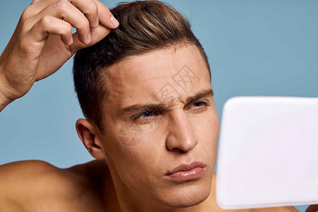 一个男人用蓝背景的眼神 照着镜子看脸男人男生皮肤成人奶油剃须护理治疗身体卫生背景图片
