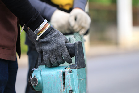 打补丁男性工人使用电动混凝土破碎机在当地城市道路 人行道 工作施工现场用手提钻挖掘和钻孔混凝土修复车道表面岩石工程破坏铺路男人石匠劳动背景