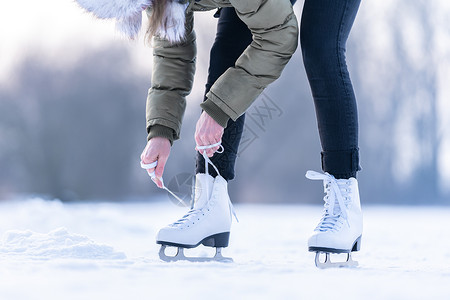 抽冰尜的女孩将冬季溜冰的鞋带绑在冰冻湖上 滑冰刀刃乐趣池塘娱乐季节天气溜冰者锻炼冒险女性背景