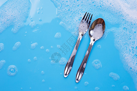 洗碗概念 用肥皂泡沫在湿蓝背景上用汤匙叉子和香皂泡沫背景