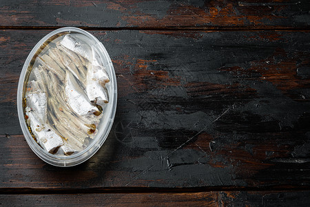 腌制的咸凤尾鱼片 在塑料容器中 在旧的深色木桌背景上 顶视图平躺 有复制空间和文本空间背景图片