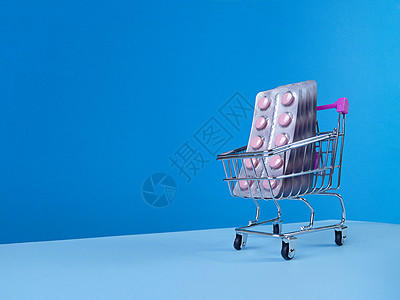 药房蓝色粉红色平板电脑在超市推车中以蓝色背景 倾斜的潮流天空线和复制空间播放背景