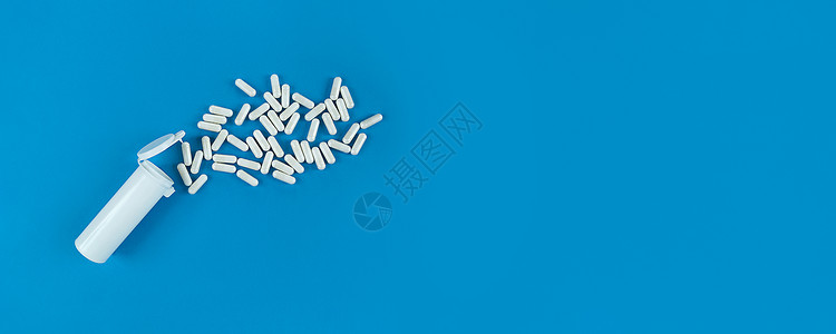 蓝色背景的白色石膏药瓶和散落的药丸胶囊 有复制空间的Banner背景图片