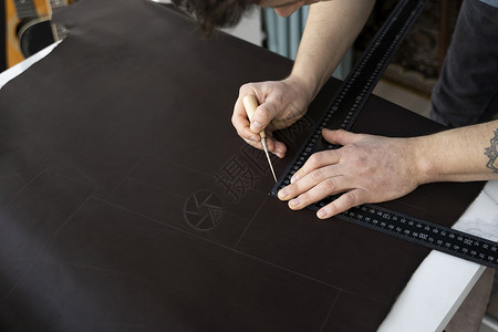 男人的手拿着锥子和金属尺子 在他的工作室里制作皮革钱包 与棕色天然皮革的工作过程 工匠拿着制作工具 在皮革上做标记配饰皮艺剪刀成产品高清图片素材