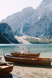 新婚夫妇乘坐木船航行在意大利的 婚礼在欧洲 在 Braies 湖上 新婚夫妇新郎用木桨划船 新娘坐在对面戏服假期夫妻婚姻景色丈夫背景