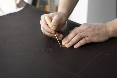 男人的手拿着锥子和金属尺子 在他的工作室里制作皮革钱包 与棕色天然皮革的工作过程 工匠拿着制作工具 在皮革上做标记制造业成人皮匠机器高清图片素材