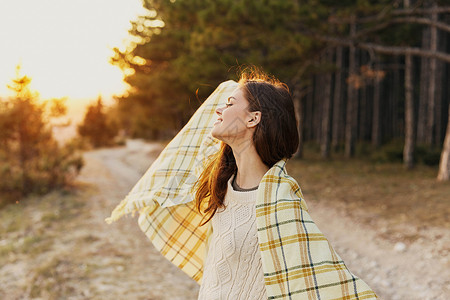 格子太阳素材带着温暖衣服在树木附近的森林里旅行的快乐女游客背景