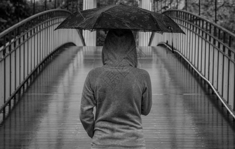 年轻女性在雨天守着保护伞 穿过木桥背景图片