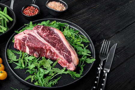 黑色蔬菜含草药和盐的牛排 黑色木制桌底 有复制文本空间;干旧 Raw T骨或门房牛肉肉背景