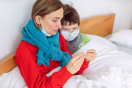 强制休息令母亲和儿子在有病毒感染的床上发烧家庭女士药品义务药物男生温度计口罩面具背景