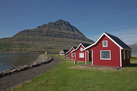 在冰岛东部爱斯基菲约尔杜尔背景中拥有强大的Holmatindur山的传统红漆木板房旅游房子海岸旅行村庄冒险峡湾吸引力风景冰川背景