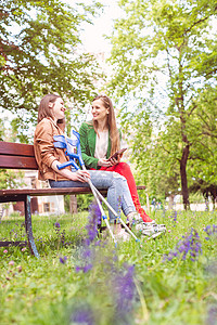 两名妇女 一名健康 一名脚扭伤 坐在长凳上闺蜜断腿公园腿部微笑长椅时间闲暇拐杖朋友背景图片