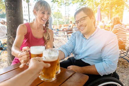 在啤酒花园喝酒的朋友 一个人坐在轮椅上餐厅女士残障乐趣帮助坐椅夫妻城市男人人士背景图片
