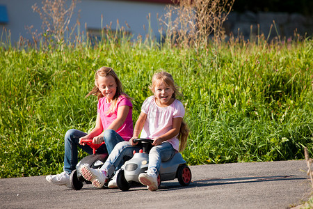 两个姐妹带着玩具车竞赛孩子快乐行动爬坡赛车乐趣驾驶享受兄弟姐妹背景图片