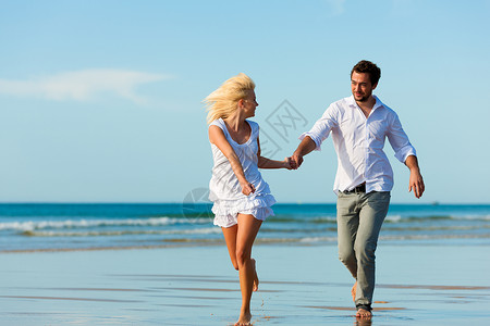 海滩上的情侣奔向辉煌的未来喜悦女朋友阳光照射丈夫蜜月男朋友快乐天空成人闲暇背景图片