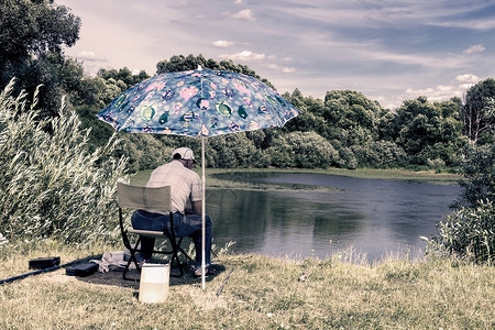 钓鱼伞一个男人在美丽的湖岸钓鱼成人倒影太阳旅行防晒天空爱好活动钓竿灌木丛背景
