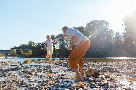 在阳光明媚的天气下 在河边玩水的 有趣的老年情侣男人活力机动性脊柱岩石老年人福利石头女性男性自然高清图片素材