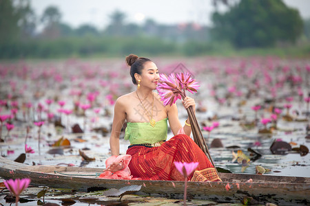 船上女孩身着传统服饰的年轻亚洲女性在船上和池塘里的粉红色莲花 穿着传统服装的漂亮女孩 泰国语 大城府 优雅装饰品文化裙子艺术女士丝绸金子背景