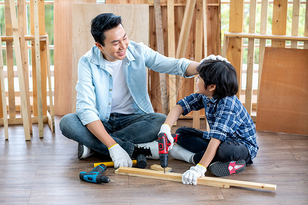 亚洲父亲在家庭木工工作场所钻木头时 心情愉快地摸着儿子的头 亚洲家庭观念留在家里 一起享受良好的关系爱好背景