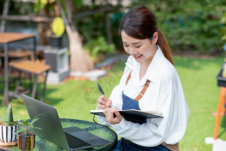 短句心情记录美丽的亚洲女性将数据记录到笔记本电脑前的笔记本中 并心情愉快地呆在家里的花园里背景