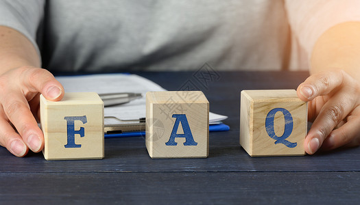 简单问题素材男性坐在一张桌子上 持有立方体 在蓝色背景的木块上输入 FAQ(经常询问的问题)背景